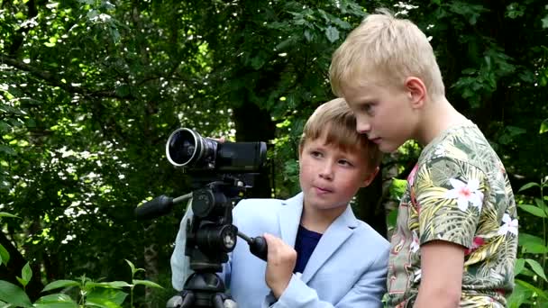 ビデオカメラを持った若い男の子が緑豊かな公園の背景の性質について映画を撮影します。. — ストック動画