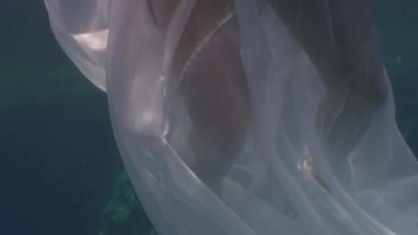 Young woman underwater model in white cloth on background of blue water. Stock Footage