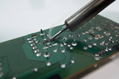 Devre kartındaki bir parçanın bacağını lehimleyen teknisyen. Elektronik onarımını kapat.