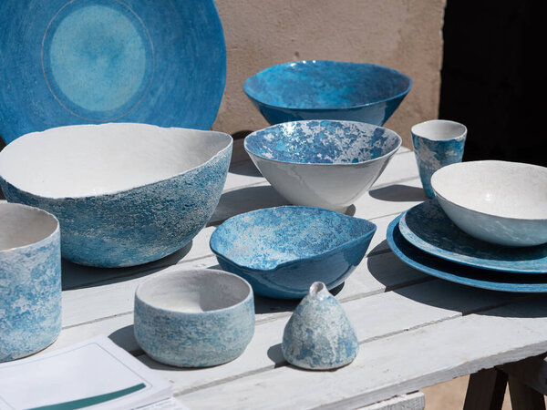 Blue and White Ceramic Plates, Vases, and Cups displayed on a Wooden Table Outdoors.