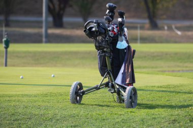 Güneşli bir günde golf sahasında tekerlekli siyah golf çantası..