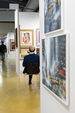 Seller of Artworks Sitting at a Desk in a Modern Art Gallery.