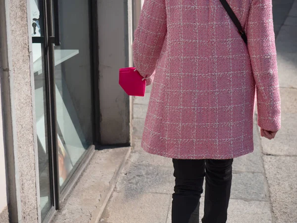 ピンクの保護マスクを持つピンクのジャケットの女性の後ろからの眺め彼女の腕に詰め込まれた通りを歩く — ストック写真