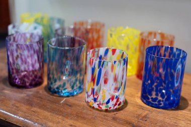 Ahşap bir rafta duran çeşitli renk ve desenlerde çok renkli camlar..