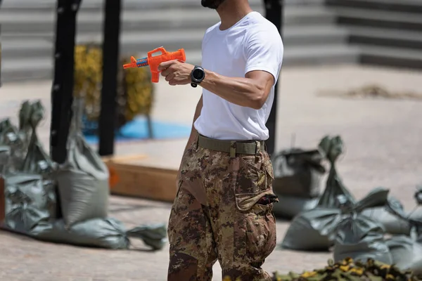 Soldier in Uniform and Camouflage Pants Playfully firing an Orange Water Gun.