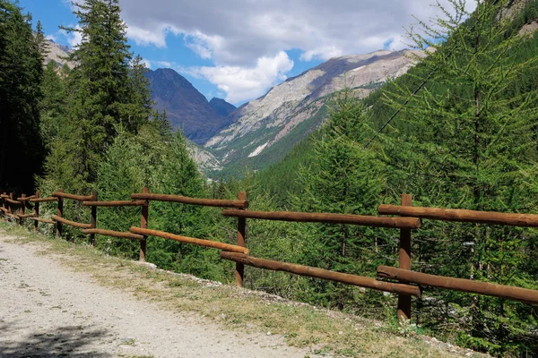 Path with Wooden Fence and in the background Mountain of the Italian Alps and Blue sky with Clouds.