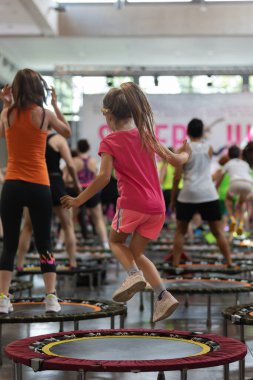 Little Girl having Fun Jumping During Fitness Workout with Rebounders: People doing Fitness Exercise in Class at Gym with Music and Teacher on Stage.
