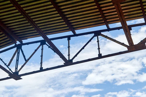 Gökyüzüne karşı gökyüzü bulutlu atölyenin çatısını destekleyen kiriş çerçevesi