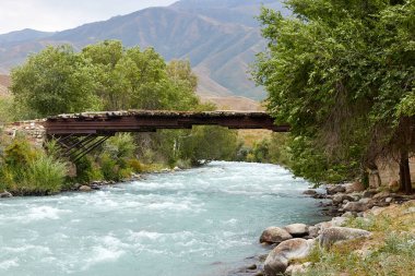 Dağ nehri üzerinde kütüklerle kaplı eski metal bir köprü.