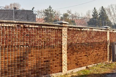 Çitin üstünde kırmızı tuğla duvar ve dikenli tel var.