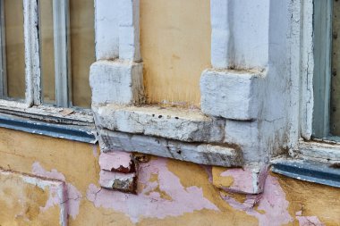 fragment of the wall of an old house with windows and peeling paint and plaster