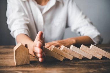 hand stopping risk the wooden blocks from falling on house, Home insurance ,security and Risk management concept.	