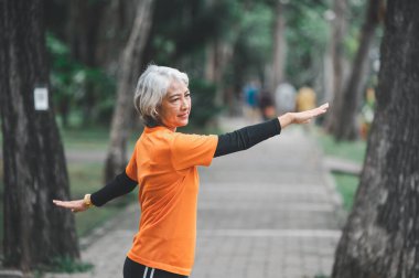 Elderly, white-haired Asian woman exercising in the park early in the morning.