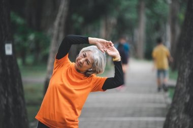 Yaşlı, beyaz saçlı Asyalı kadın sabahın erken saatlerinde parkta egzersiz yapıyor..