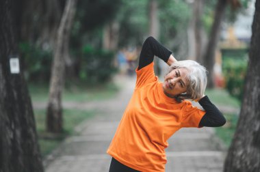 Yaşlı, beyaz saçlı Asyalı kadın sabahın erken saatlerinde parkta egzersiz yapıyor..