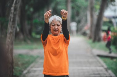 Yaşlı, beyaz saçlı Asyalı kadın sabahın erken saatlerinde parkta egzersiz yapıyor..