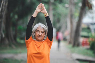 Yaşlı, beyaz saçlı Asyalı kadın sabahın erken saatlerinde parkta egzersiz yapıyor..