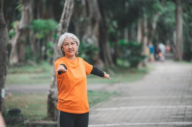 Yaşlı, beyaz saçlı Asyalı kadın sabahın erken saatlerinde parkta egzersiz yapıyor..