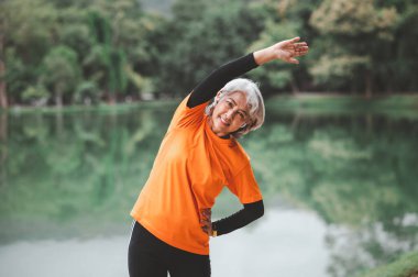 Yaşlı, beyaz saçlı Asyalı kadın sabahın erken saatlerinde parkta egzersiz yapıyor..
