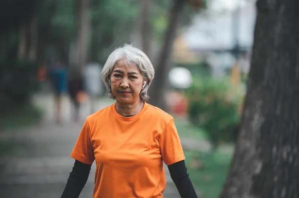 Elderly, white-haired Asian woman exercising in the park early in the morning.