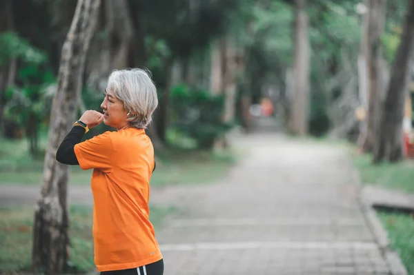 Elderly, white-haired Asian woman exercising in the park early in the morning.