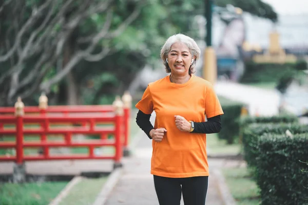 Elderly, white-haired Asian woman exercising in the park early in the morning.