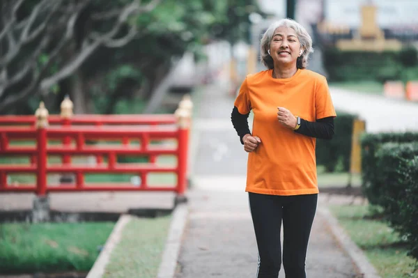 Elderly, white-haired Asian woman exercising in the park early in the morning.