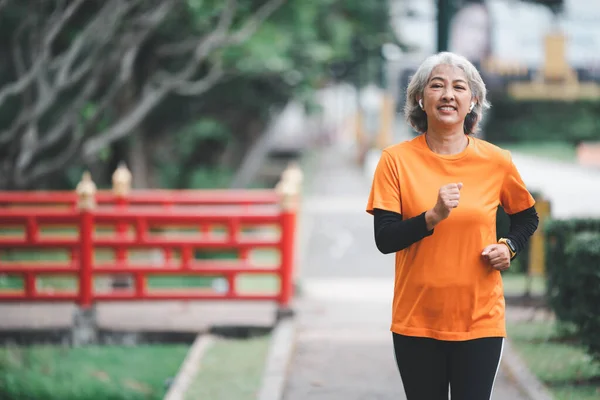 Elderly, white-haired Asian woman exercising in the park early in the morning.