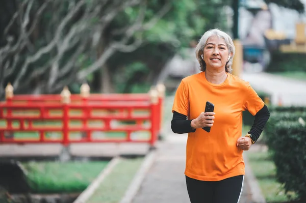 Elderly, white-haired Asian woman exercising in the park early in the morning.