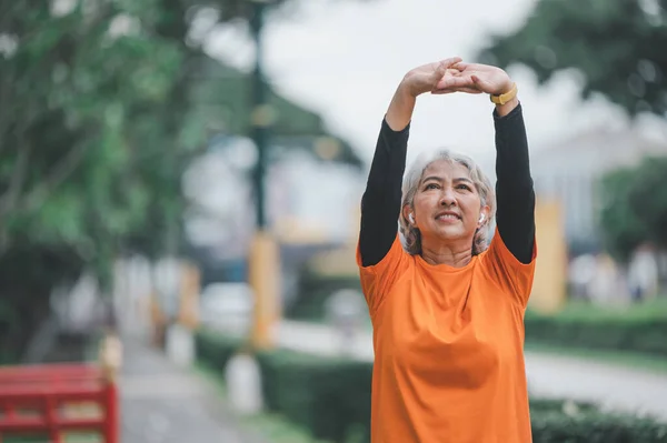 Elderly, white-haired Asian woman exercising in the park early in the morning.