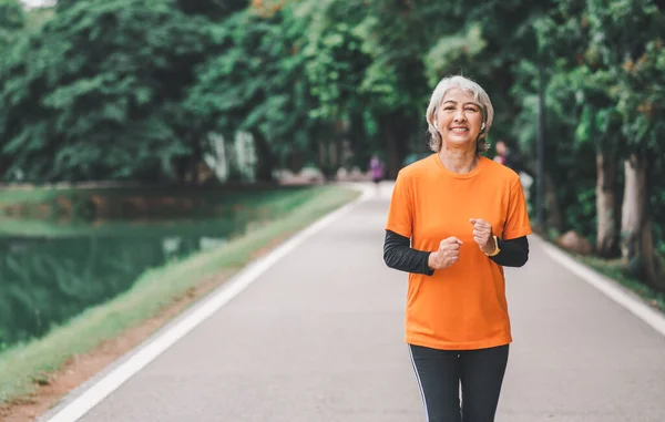 Elderly, white-haired Asian woman exercising in the park early in the morning.