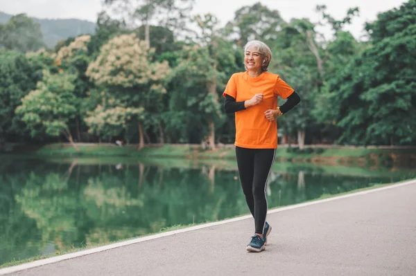 Elderly, white-haired Asian woman exercising in the park early in the morning.