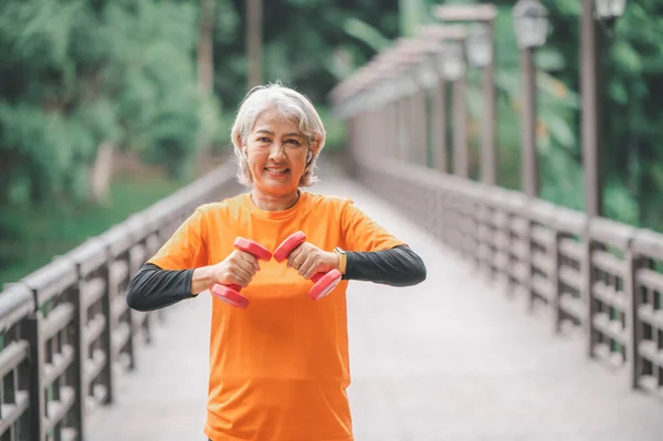 Elderly, white-haired Asian woman exercising in the park early in the morning.