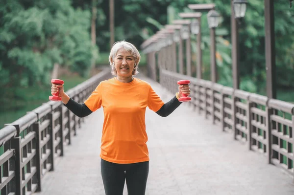 Elderly, white-haired Asian woman exercising in the park early in the morning.