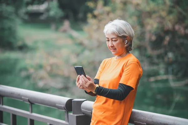 Elderly white haired Asian woman talking Video call while exercising in the park in the morning.