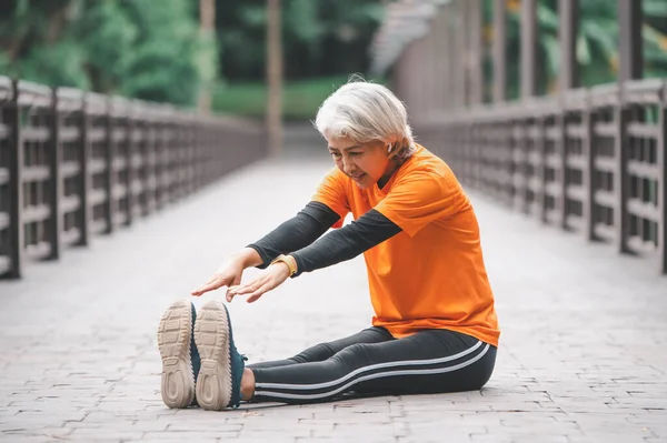 Elderly, white-haired Asian woman exercising in the park early in the morning.