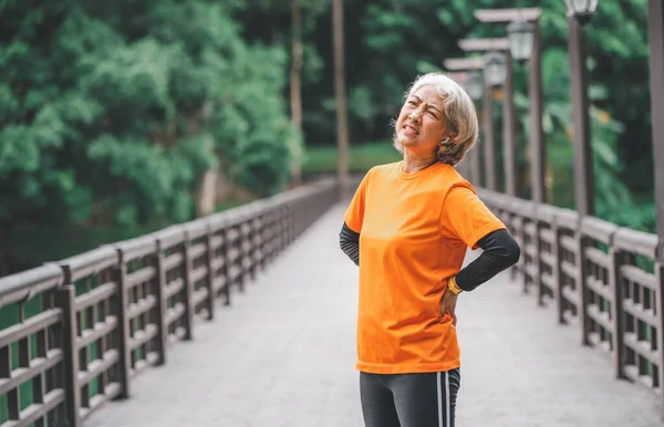 elderly, white-haired Asian woman has a backache while exercising in the park in the morning.