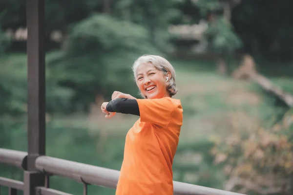 Elderly, white-haired Asian woman exercising in the park early in the morning.