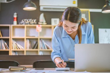 İş yapan Asyalı kadın çalışmak için hesap makinesini kullanarak ofiste masa başında oturuyor. İş Konsepti Analizi ve Planlaması