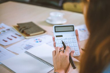İş yapan Asyalı kadın çalışmak için hesap makinesini kullanarak ofiste masa başında oturuyor. İş Konsepti Analizi ve Planlaması