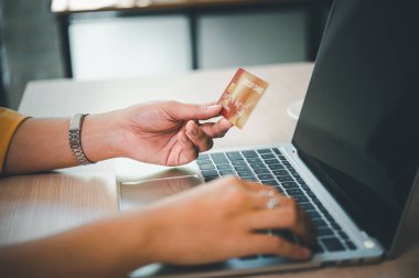 Kredi kartı tutan ve dizüstü bilgisayar kullanan genç bir kadın. Kafede çalışan bir iş kadını. Çevrimiçi alışveriş, e-ticaret, internet bankacılığı, harcama
