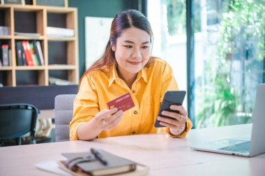 Kredi kartı tutan ve dizüstü bilgisayar kullanan genç bir kadın. Kafede çalışan bir iş kadını. Çevrimiçi alışveriş, e-ticaret, internet bankacılığı, harcama