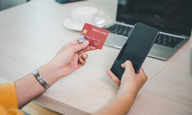 Kredi kartı tutan ve dizüstü bilgisayar kullanan genç bir kadın. Kafede çalışan bir iş kadını. Çevrimiçi alışveriş, e-ticaret, internet bankacılığı, harcama