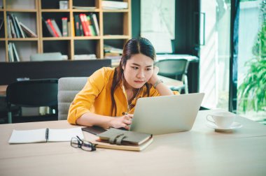 Bir kafede dizüstü bilgisayarıyla çalışan yorgun ve sıkılmış bir iş kadını.