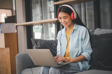 İnternette kulaklık takan genç bir öğrenci, video aracılığıyla sohbet, evdeki kanepede uzaktan öğrenme.