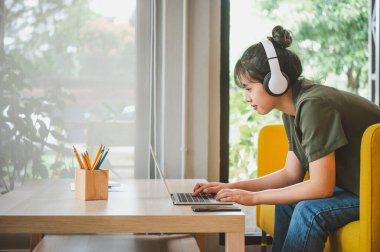 Kulaklık takan genç bir kadın müzik dinlerken, oyun oynarken, kanepede rahatça sipariş verirken telefonuna oturuyor..