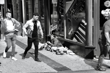 Cardiff, Galler 31 Temmuz 2021: Cardiff şehir merkezindeki kaldırımda oturan genç, evsiz bir kadının yanından geçen tek renkli fotoğraf. Giysiler ve aidiyet, zenginlik boşluğunu vurguluyor. 