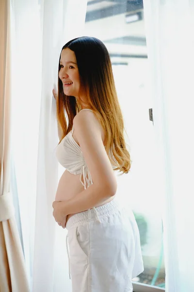 ウィンドウで大きな腹を持つ幸せな妊娠中の女性の立って若い美しい妊婦 妊婦の笑顔 — ストック写真