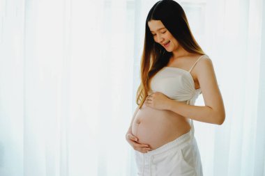 Pencerede kocaman göbekli mutlu hamile bir kadının önünde duran güzel, hamile bir kadın. Gülümseyen hamile kadın.