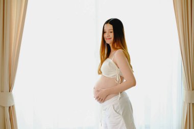 Pencerede kocaman göbekli mutlu hamile bir kadının önünde duran güzel, hamile bir kadın. Gülümseyen hamile kadın. beyaz arkaplan.